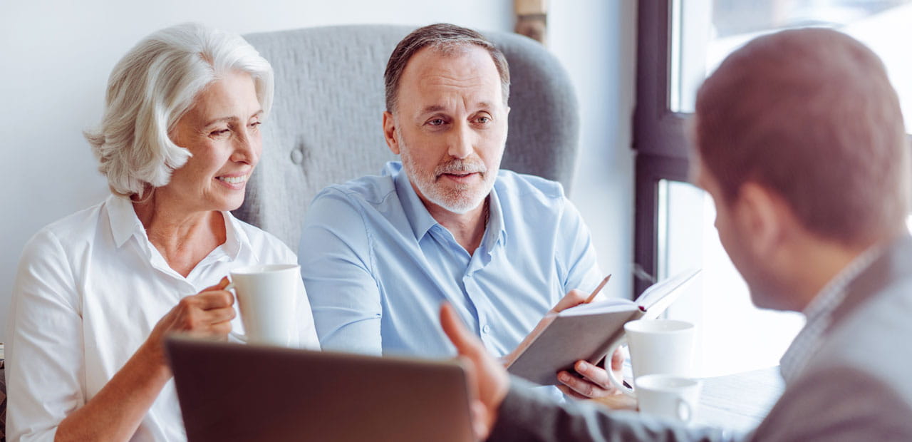 elderly couple reviewing notebook with business professonal