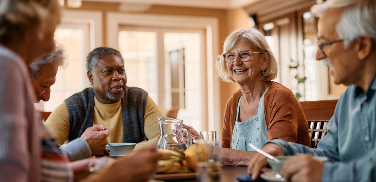 Group of senior friends communicating while eating lunch in nursing home.