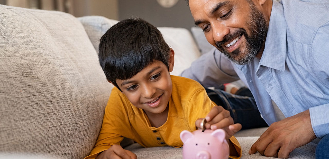 Happy indian son saving money in piggy bank with father