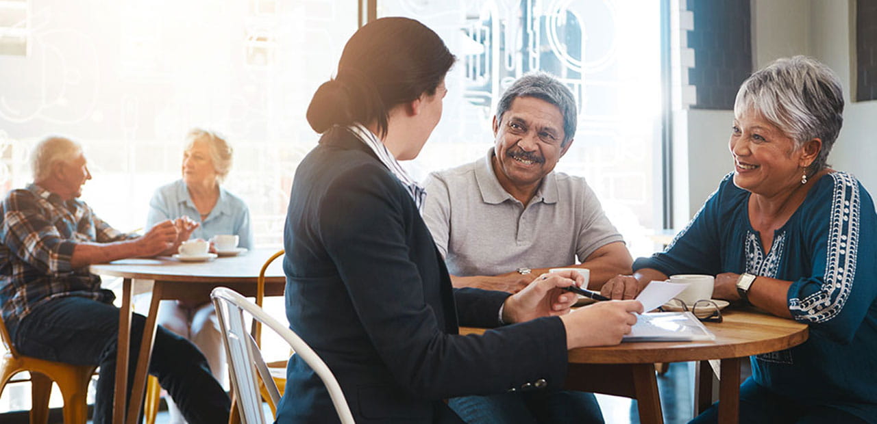 An elderly couple having a conversation with a professional. Another elderly couple sitting in the background.